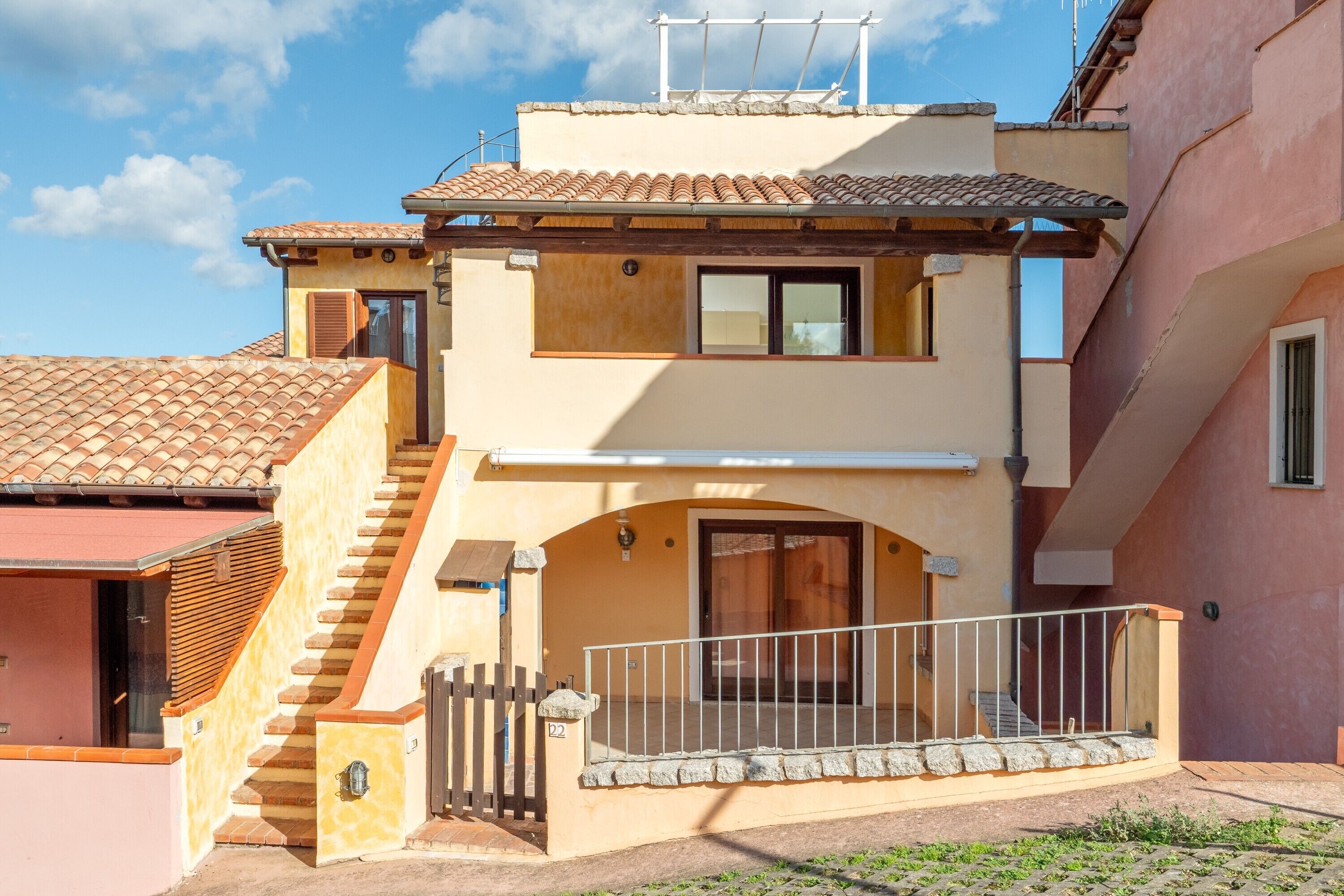 Un bâtiment à deux étages, doté d’un toit recouvert de tuiles, d’un balcon avec une rambarde en métal et d’un escalier menant à l’entrée.