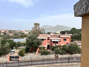 Zona residencial costera con un edificio rosa destacado, una masa de agua y montañas al fondo.