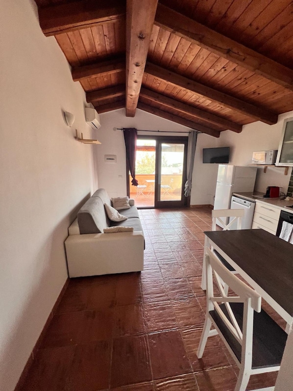Una habitación acogedora con techo de madera, un sofá, una mesa de comedor y una zona de cocina.