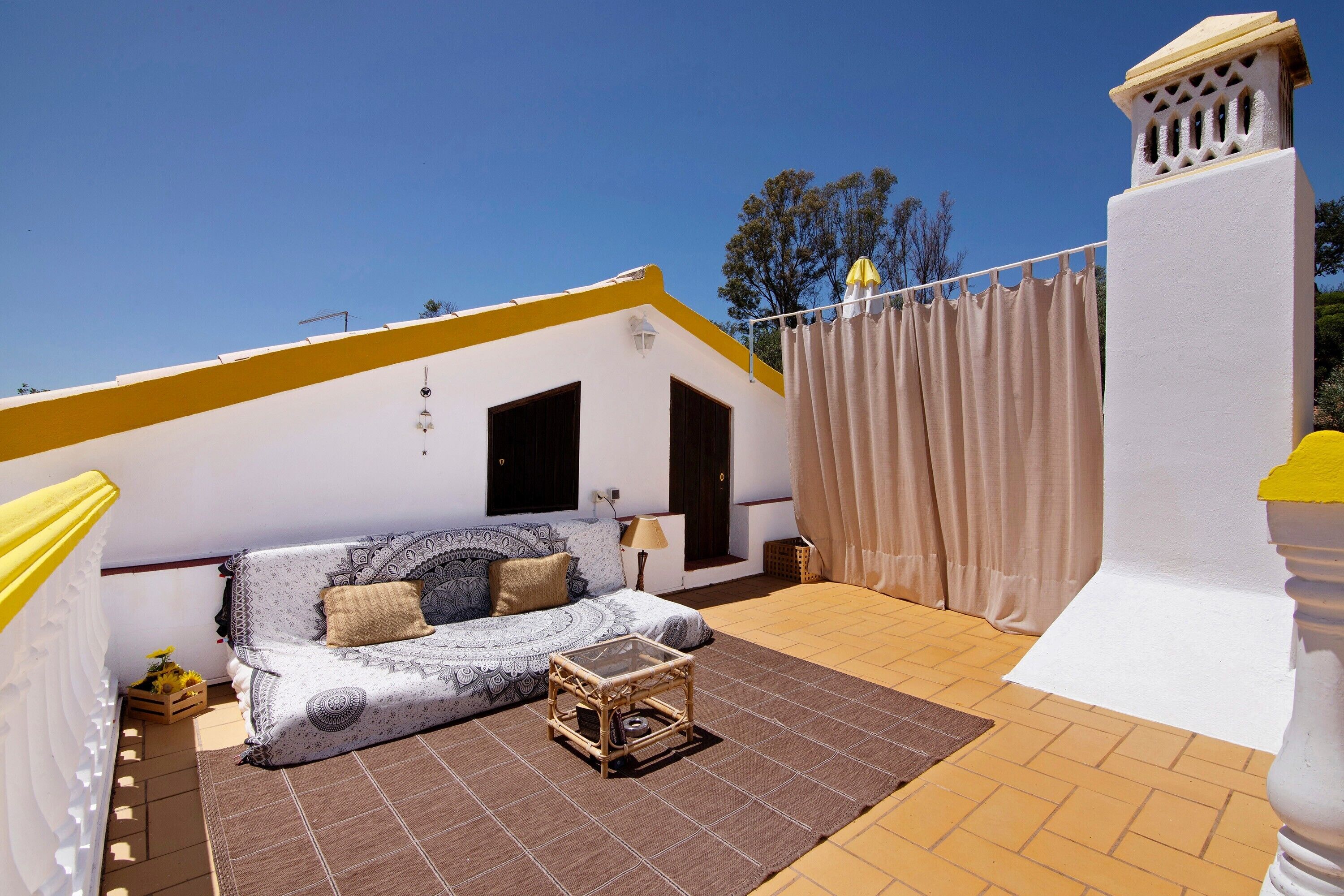 A sunlit patio with a sofa, a small table, and a white wall with a window.