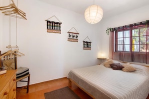 A bedroom with a bed, a hanging light fixture, a window with curtains, and wall decorations.