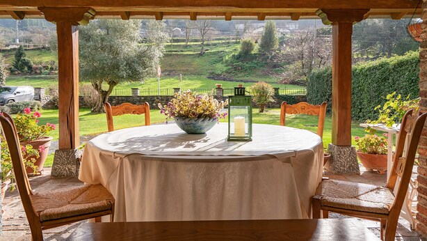 A covered outdoor seating area with a round table, chairs, and a potted plant.