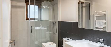 A modern bathroom with a glass-enclosed shower, a white toilet, and a large sink.