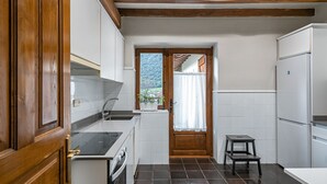 A compact kitchen with white cabinets, a built-in oven, a sink, and a small stool.