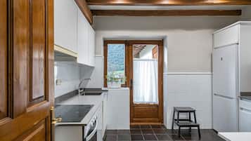 Une cuisine compacte avec des meubles blancs, un four encastré, un évier et un petit tabouret.