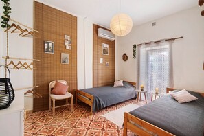 Una habitación con dos camas, una silla, una mesita, una planta colgante y una ventana con cortinas.
