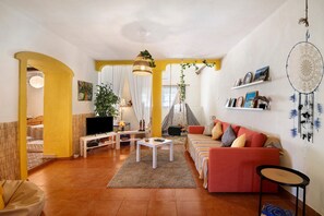 Una sala de estar con sofá, televisor y una planta colgante.