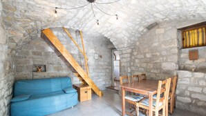 A stone-walled room with a wooden staircase, a blue sofa, and a wooden dining table with chairs. - Holiday Home 'Gite De L'écurie' with Air Conditioning (Berrias-et-Casteljau)