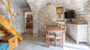 A rustic stone interior with a wooden dining table, chairs, a TV mounted on the wall, and a staircase. - Holiday Home 'Gite De L'écurie' with Air Conditioning (Berrias-et-Casteljau)