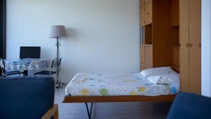Quarto com cama, escrivaninha com computador, luminária e guarda-roupa.