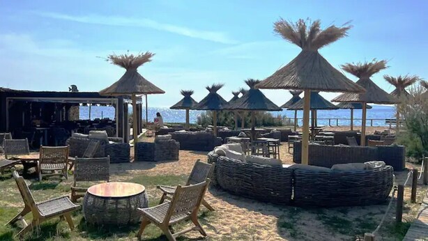 Um espaço de relaxamento à beira-mar, com assentos ao ar livre, guarda-sóis e vista para o mar.