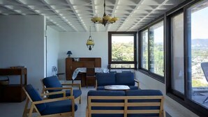 Quarto moderno com um banco de madeira, um sofá, uma escrivaninha e uma grande janela com vista para o exterior.