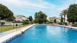 En rektangulär swimmingpool med en kant av kakel, omgiven av ett staket, och med bostadshus och träd som bakgrund.