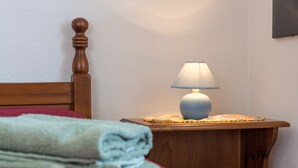 Ein ordentlich bezogenes Bett mit roter Decke, einem Holzkopfteil und einem Nachttisch mit Lampe.