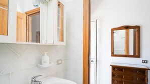 Ein Badezimmer mit weißem Waschbecken, einem Spiegel und einem Holzschrank.