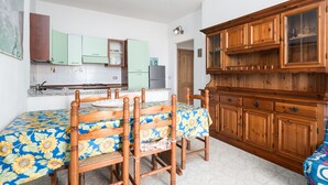 A dining area with a table set for four, wooden chairs, a cabinet with glass doors, and a kitchen in the background. - Apartment 'Posada Porto' with Private Terrace (San Giovanni)