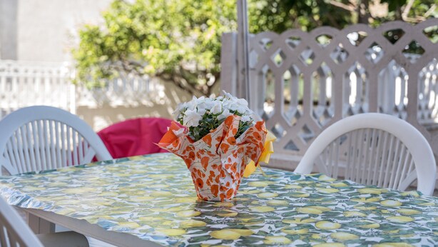 A table with a patterned tablecloth, a white chair, and a vase with flowers. - Apartment 'Posada Porto' with Private Terrace (San Giovanni)