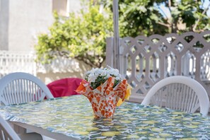 Una mesa con mantel estampado, una silla blanca y un florero con flores.
