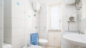 A bathroom with white tiles, a sink, a toilet, a bidet, and a window with a curtain. - Apartment 'Posada Porto' with Private Terrace (San Giovanni)