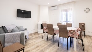 Een moderne woonkamer met een bank, een eettafel met stoelen, een flatscreentelevisie aan de muur en een open haard.