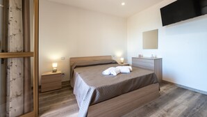 Een moderne slaapkamer met een bed, nachtkastjes, een televisie en een spiegel.