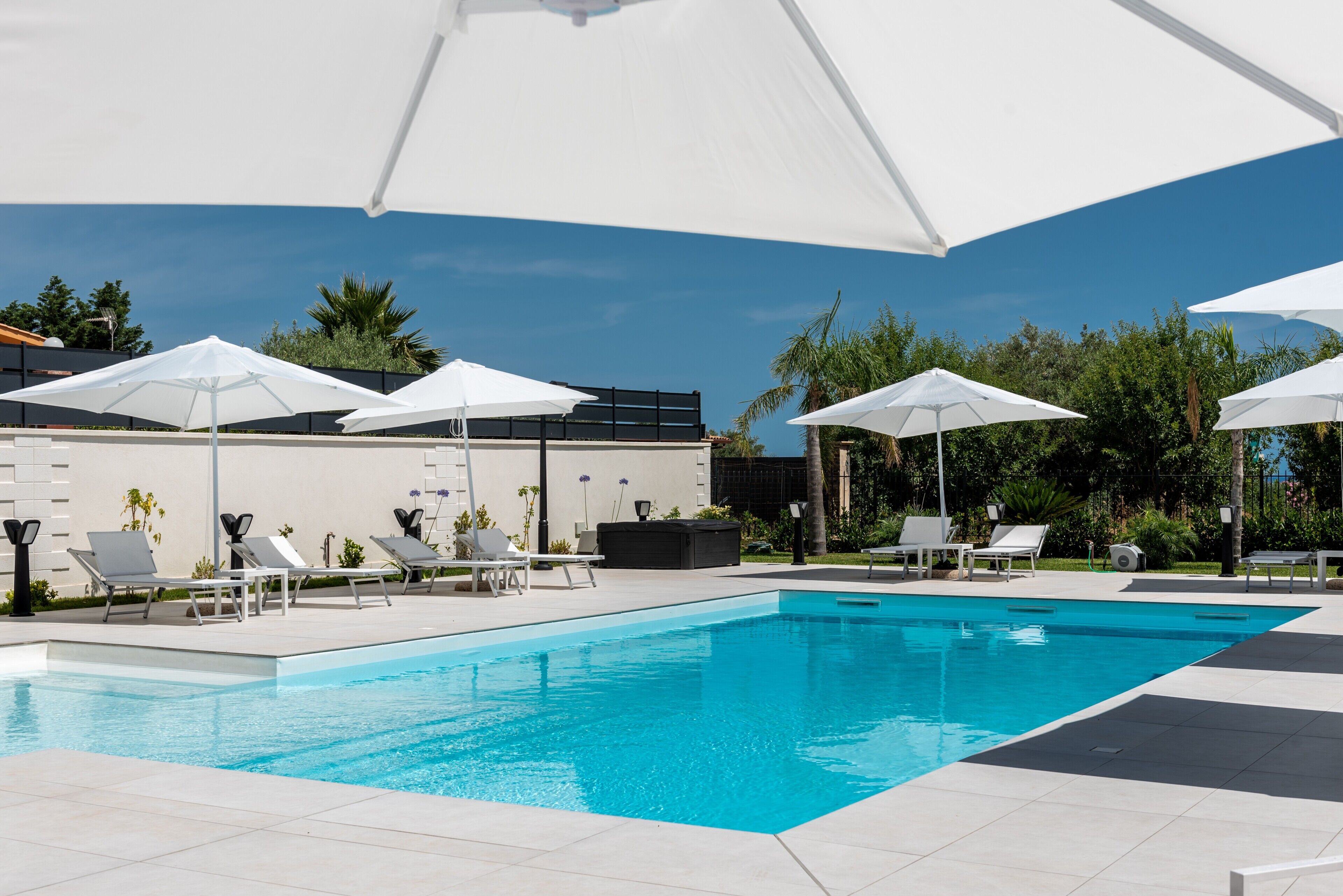 Una piscina con sombrillas blancas, sillas de descanso y un edificio al fondo.