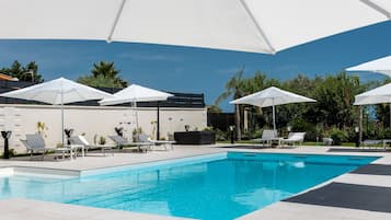 Una piscina con sombrillas blancas, sillas de descanso y un edificio al fondo.