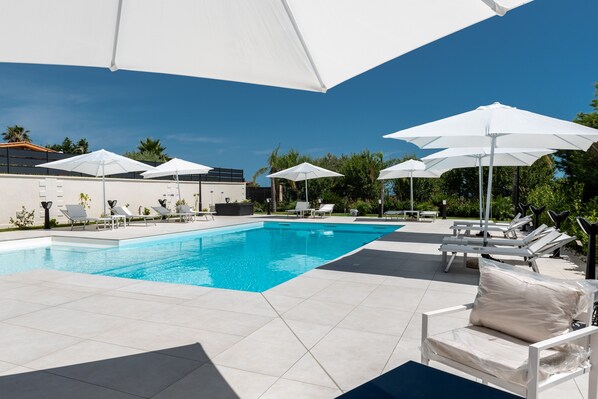 Une piscine bordée de parasols blancs et de chaises longues, le tout entouré d’une terrasse carrelée.
