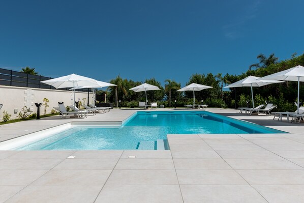 A swimming pool with white umbrellas and lounge chairs.