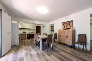 A dining area with a table and chairs, a wooden cabinet, and a kitchen in the background.