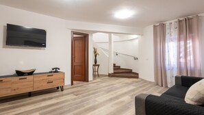 Un salon avec un canapé, un téléviseur, un meuble en bois et un escalier.