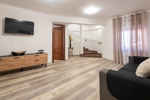 A living room with a sofa, a TV, a wooden cabinet, and a staircase.