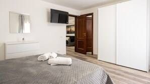 Une chambre à coucher avec un lit, un téléviseur fixé au mur, une porte en bois et une armoire blanche.