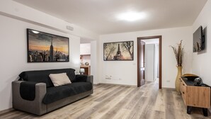 Un salon moderne avec un canapé gris, un plancher en bois et deux œuvres d’art encadrées représentant des paysages urbains.