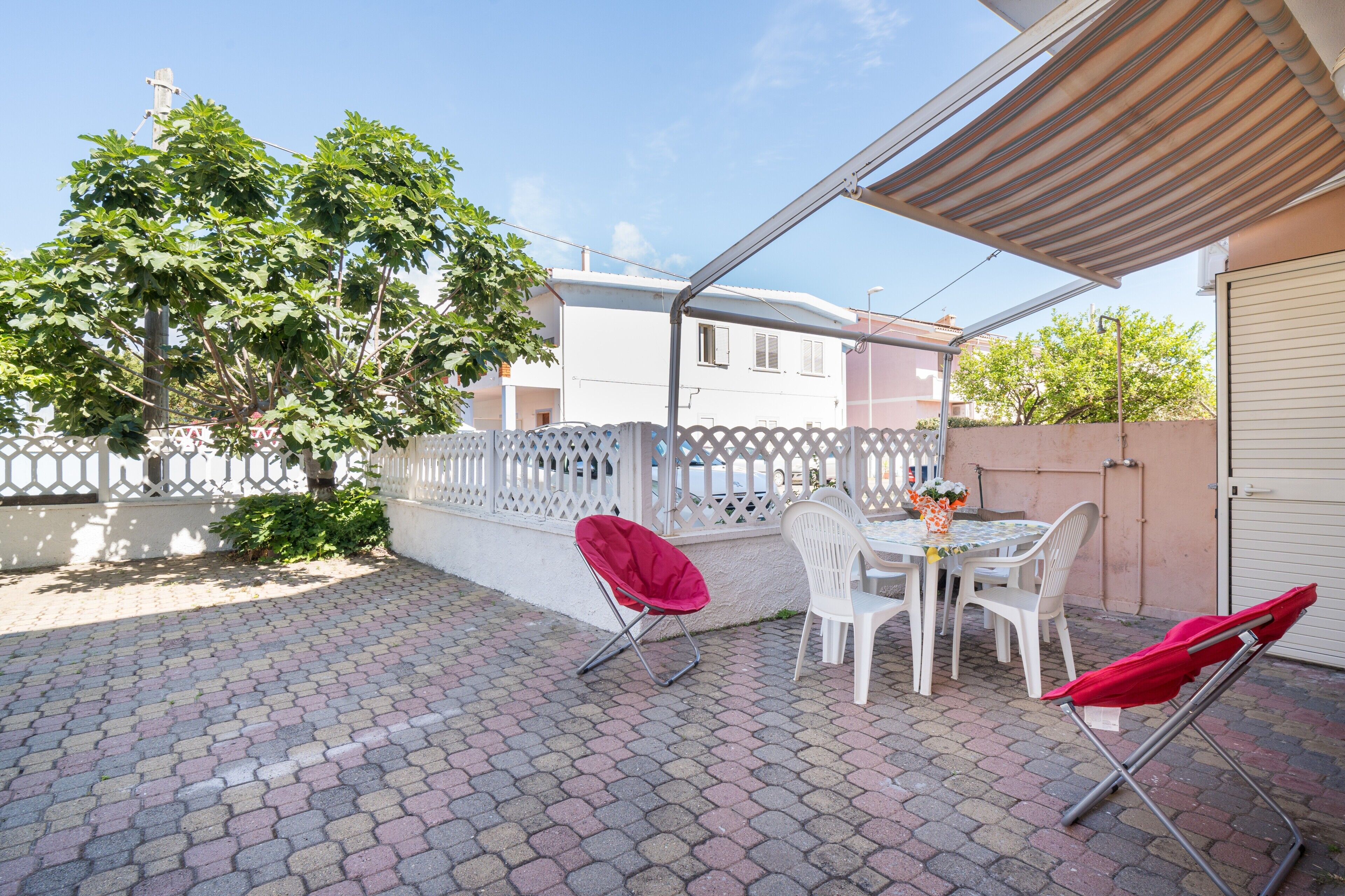 Eine Terrasse mit Tisch und Stühlen, einem roten Sonnenschirm und einem weißen Zaun.