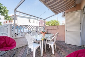 Een terras buiten met een tafel, stoelen en een overdekt gedeelte.