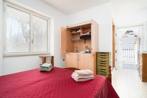 Een slaapkamer met een rode sprei, een houten garderobe, een klein tafeltje en een raam met gordijnen.