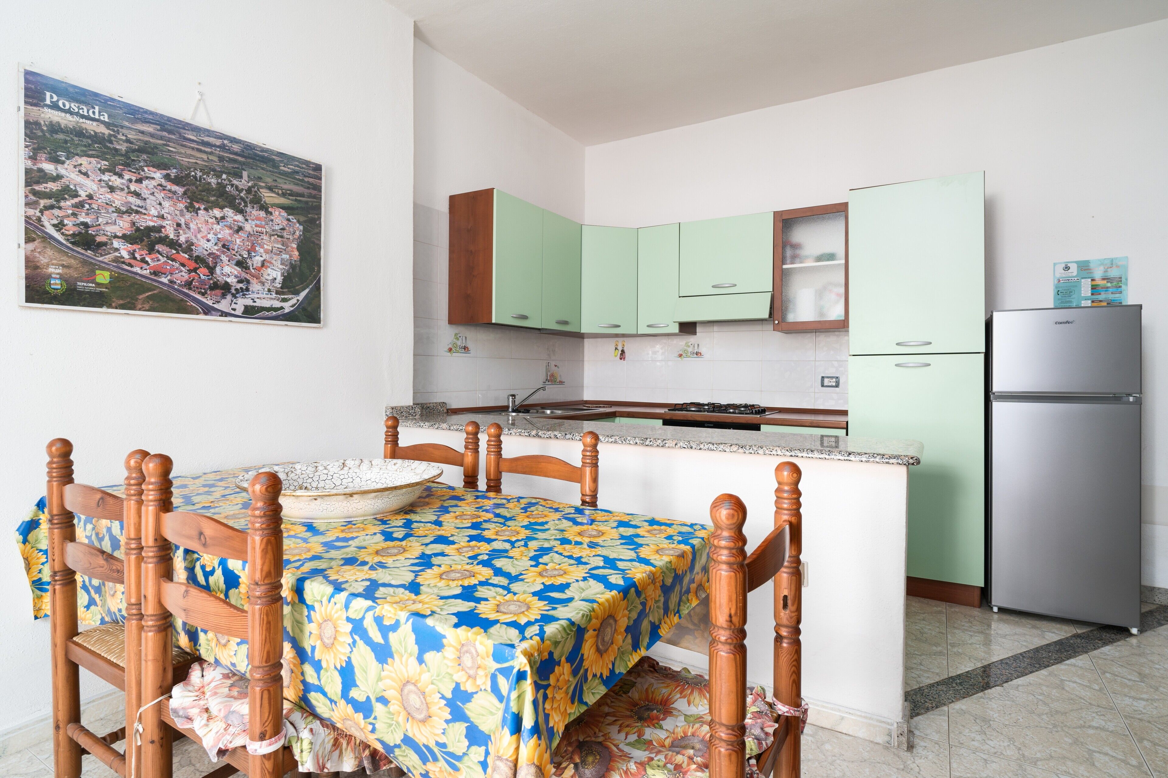 Une cuisine avec un coin repas, un réfrigérateur et un tableau accroché au mur.