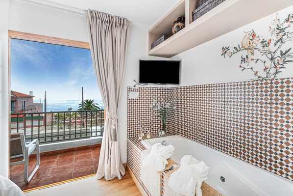 Un baño moderno con bañera, televisión y balcón con vistas al mar.