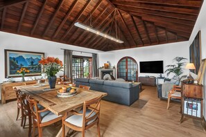 Un vaste espace de vie doté d’un haut plafond en bois, d’une table à manger avec des chaises, d’un canapé, d’une télévision et d’une cheminée.