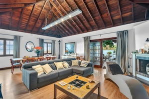 Un salon spacieux avec un plafond en bois, un canapé gris, une table basse en bois et une cheminée.