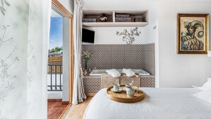 Ein Hotelzimmer mit einem Bett, einem Holztablett mit Tassen, einem an der Wand befestigten Regal mit Dekoration, einem Gemälde und Blick nach draußen.
