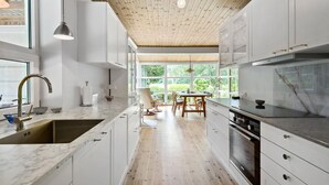 Une cuisine moderne avec des meubles blancs, un plafond en bois et de grandes fenêtres donnant sur un paysage verdoyant.
