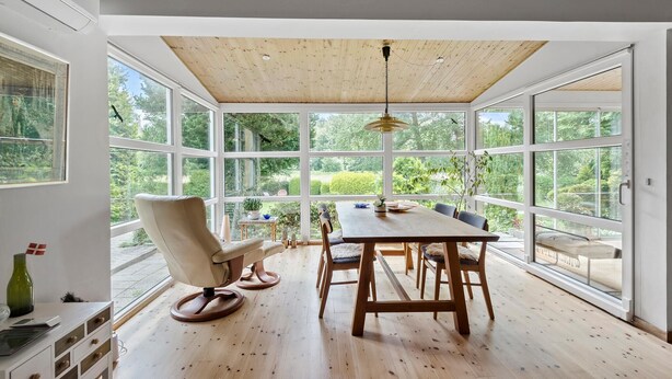 Un espace repas avec une table et des chaises en bois, de grandes fenêtres et un plafond avec des poutres apparentes.