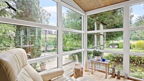 Une véranda avec une chaise blanche, une petite table sur laquelle sont posés des livres et une plante, et une vue sur un jardin.