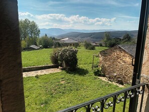 Blick von einem Balkon auf ein grünes Feld mit Steingebäuden und ferne Berge.