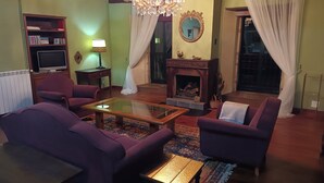 Ein Wohnzimmer mit Kamin, einer Chandelierleuchtre und violetten Möbeln.