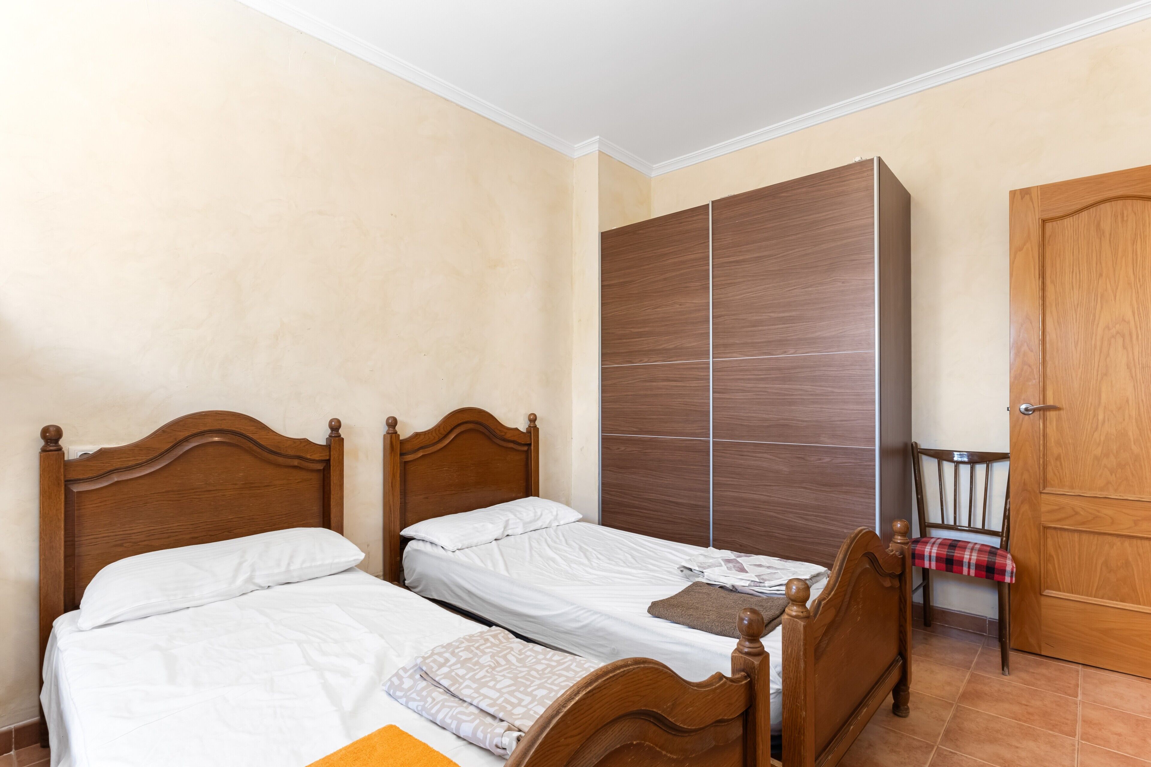A bedroom with two wooden beds, a wardrobe, and a chair.