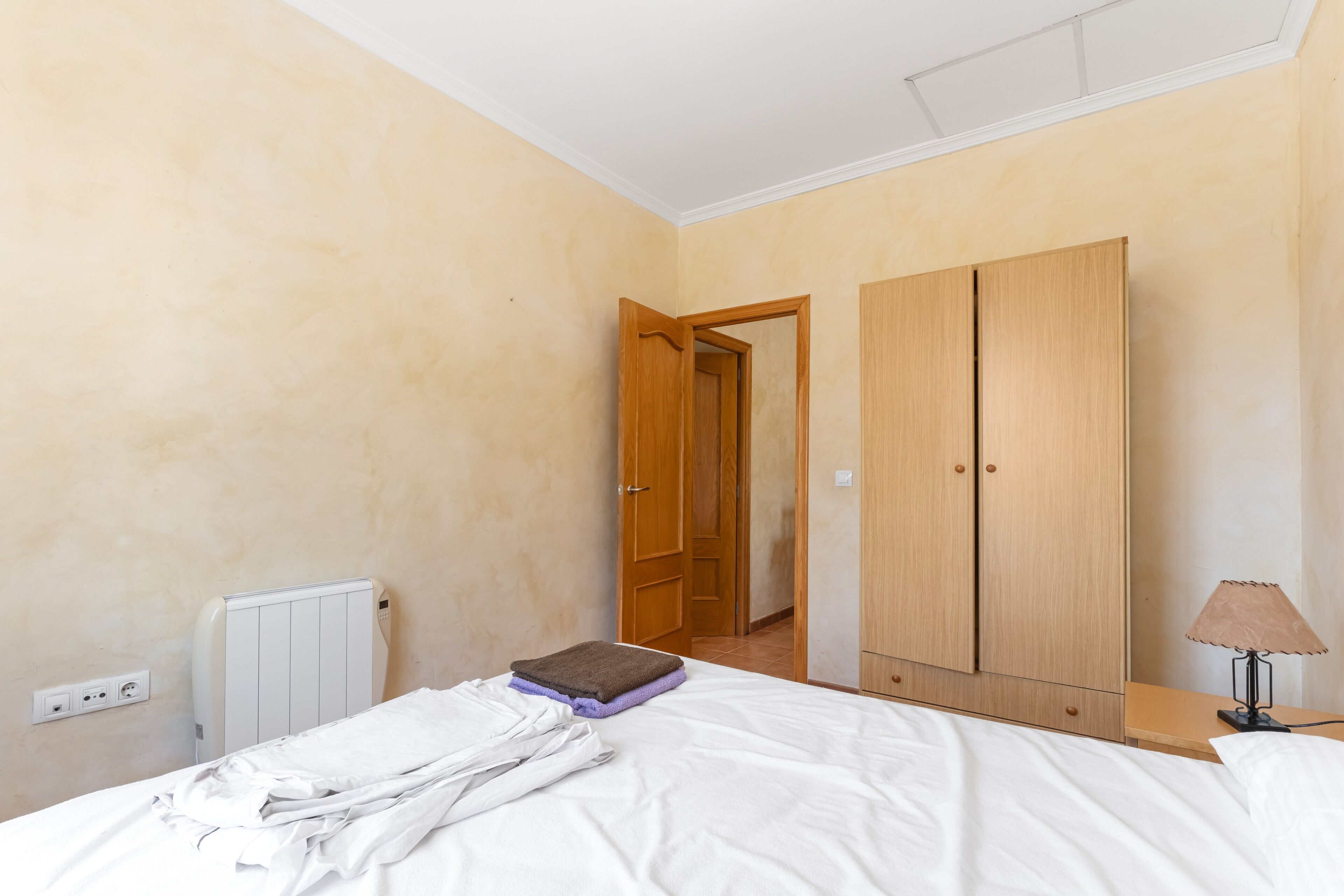 Een slaapkamer met een bed, een kast, een radiator en een lamp.