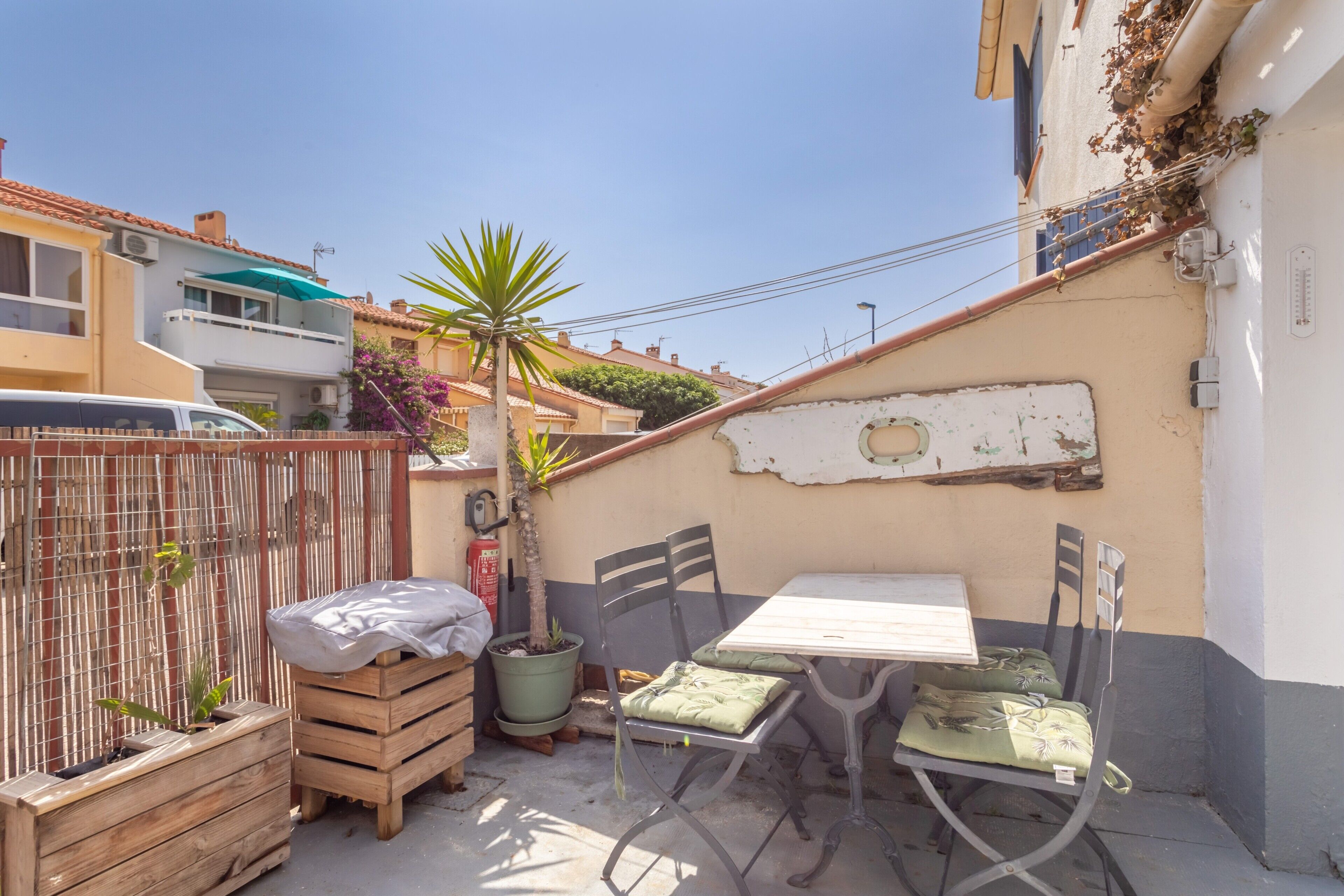 Une terrasse avec une table et des chaises, un pot de fleurs et une caisse en bois.